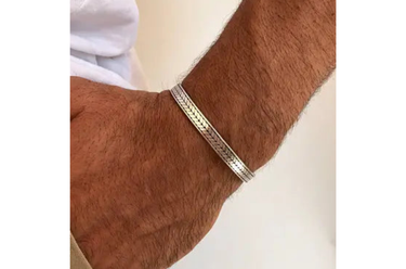 A close-up of a person's hairy wrist wearing a silver-toned metal bangle bracelet.