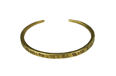 A hammered gold-tone metal cuff bracelet on a plain white background.