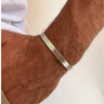 A close-up of a person's hairy wrist wearing a silver-toned metal bangle bracelet.