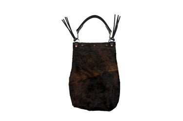 A dark brown hair-on hide shoulder bag with black leather straps, silver-tone hardware, and long black leather fringe tassels, shown against a plain white background.