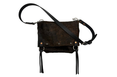 A dark brown hair-on hide shoulder bag with black leather straps, silver-tone hardware, and long black leather fringe tassels, shown against a plain white background.